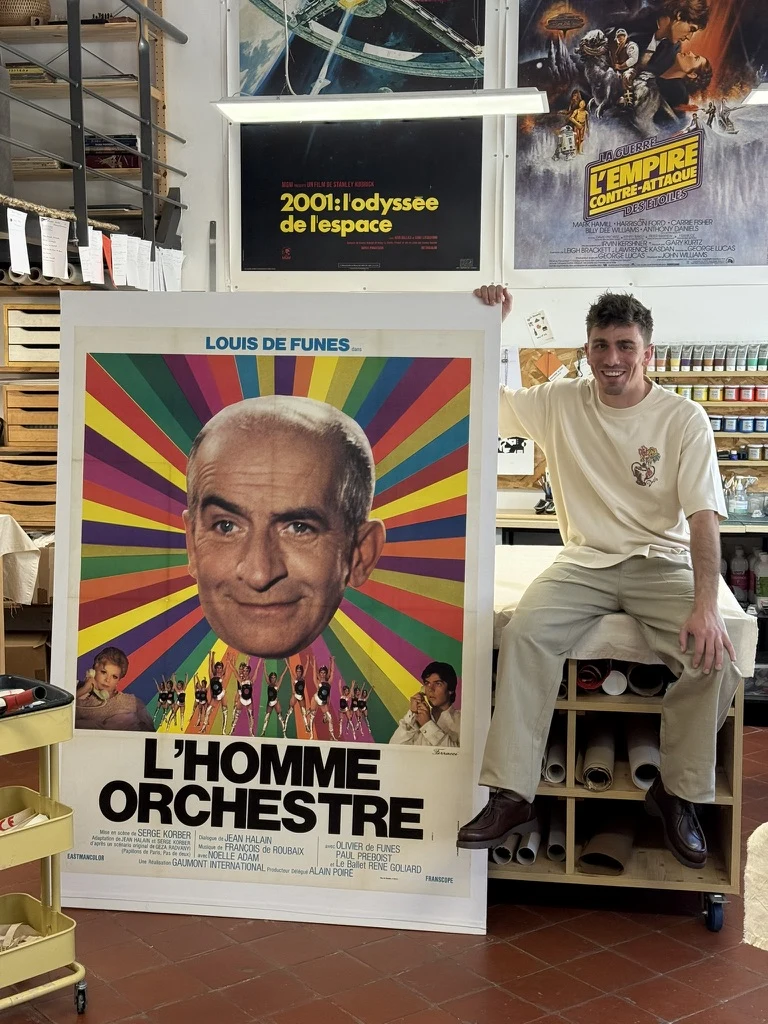Arthur dans l'atelier de L'Affiche Française, devant une affiche de L'Homme orchestre